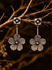 Oxidised silver floral drop earrings hanging from a dry wooden branch against dark background