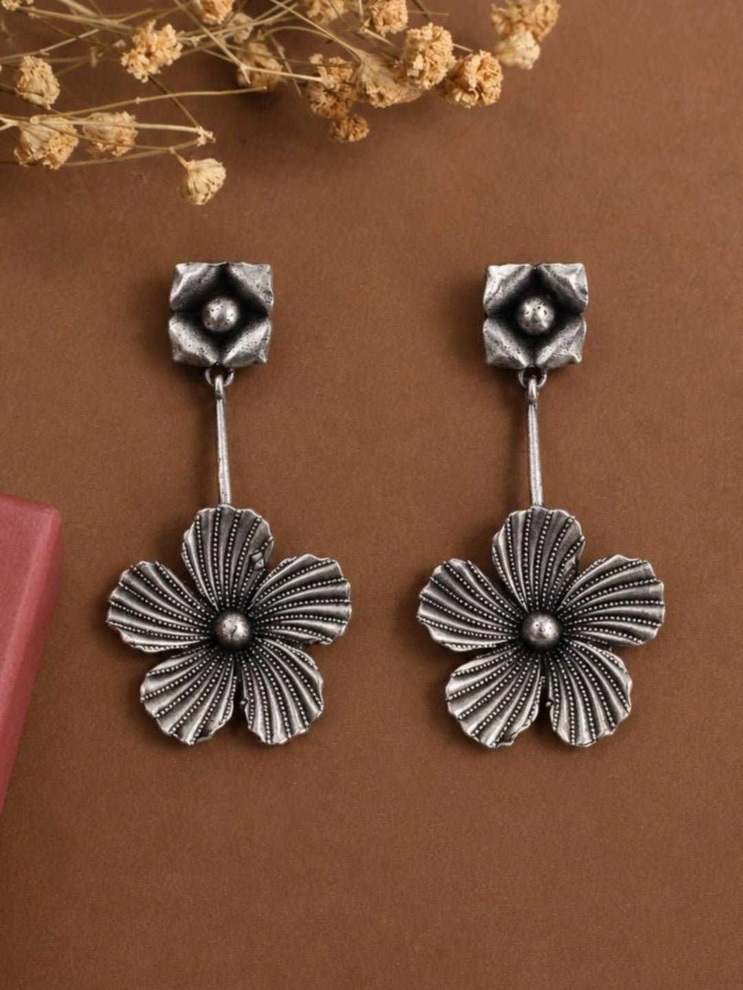 Close-up of oxidised silver floral drop earrings on brown surface showing ridged petal texture
