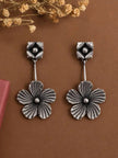 Close-up of oxidised silver floral drop earrings on brown surface showing ridged petal texture