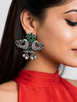 Model wearing one oxidised silver peacock stud earring with green stones and dangling ghungroo bells, dressed in a red top with dark hair