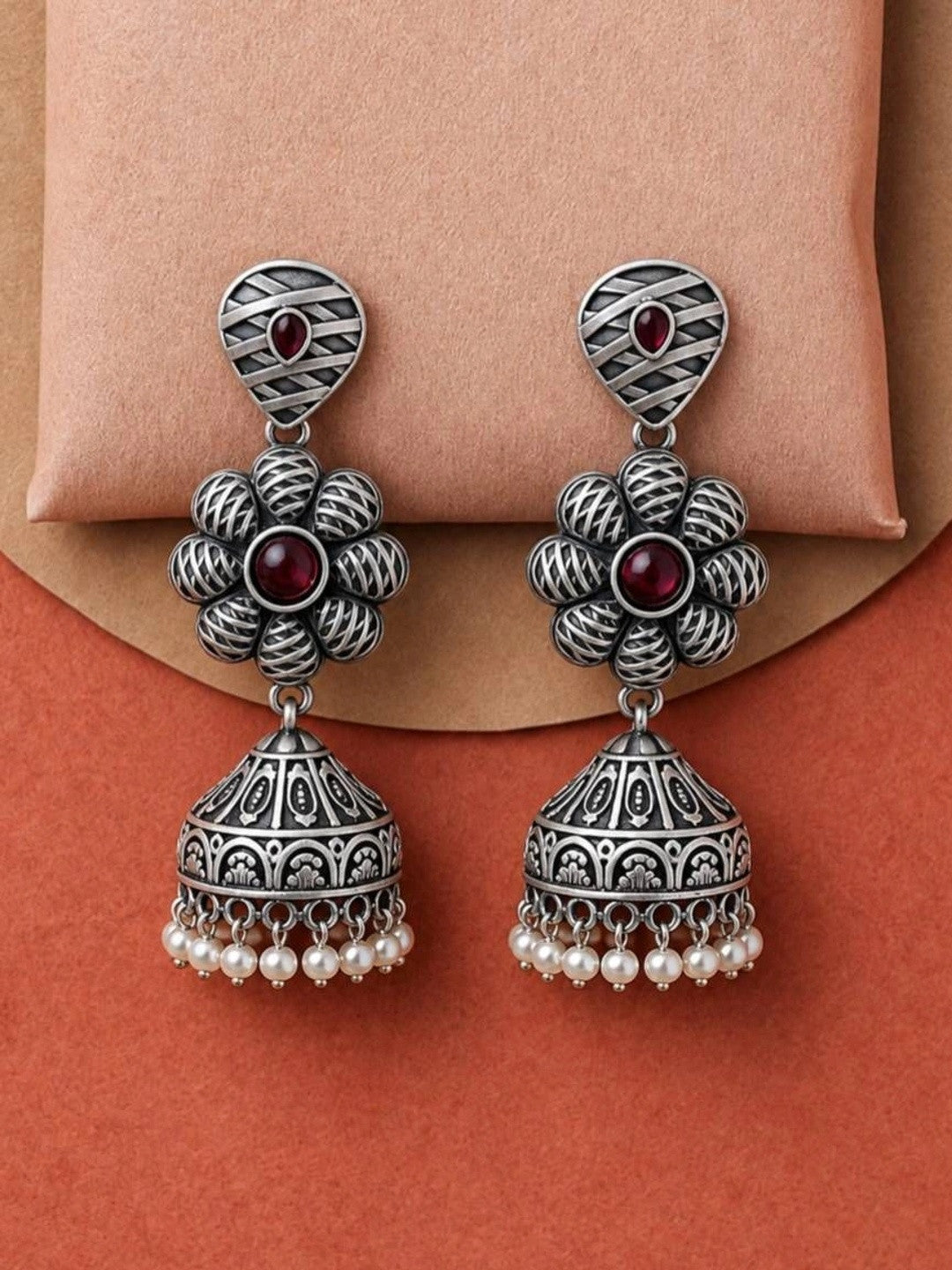 Front view of oxidised silver jhumka earrings with floral centre and dangling pearl drops on display stand