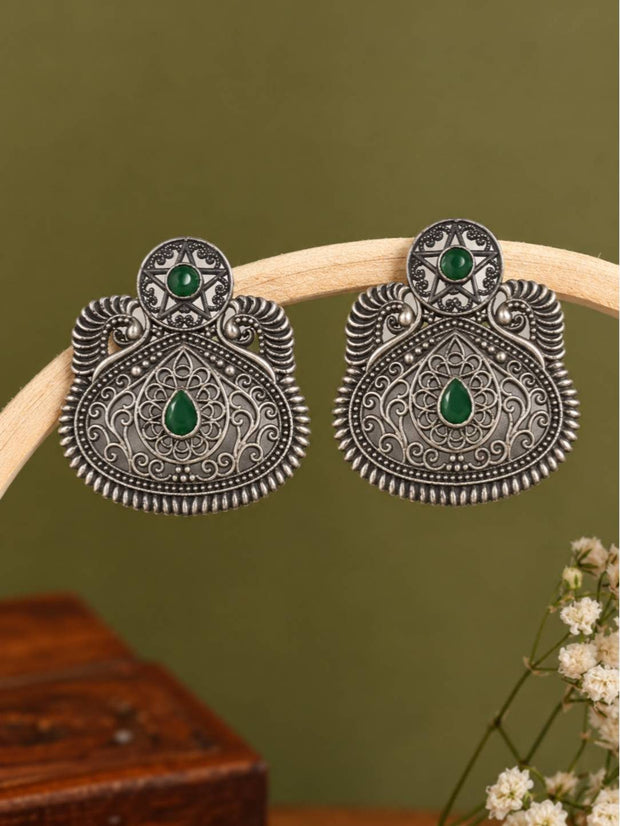Pair of oxidised silver chandbali stud earrings with green stone displayed on a wooden arc stand