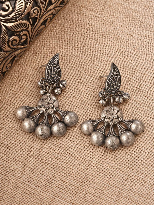 Front view of oxidised silver ghungroo earrings with floral connector and paisley tops laid flat on beige fabric
