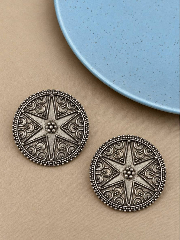 Two oxidised silver disc stud earrings with eight-pointed star motif on beige surface
