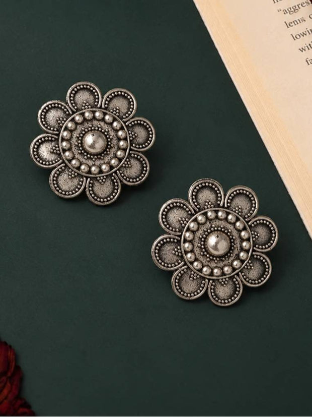 Two oxidised silver floral stud earrings placed flat on a dark green surface beside a book