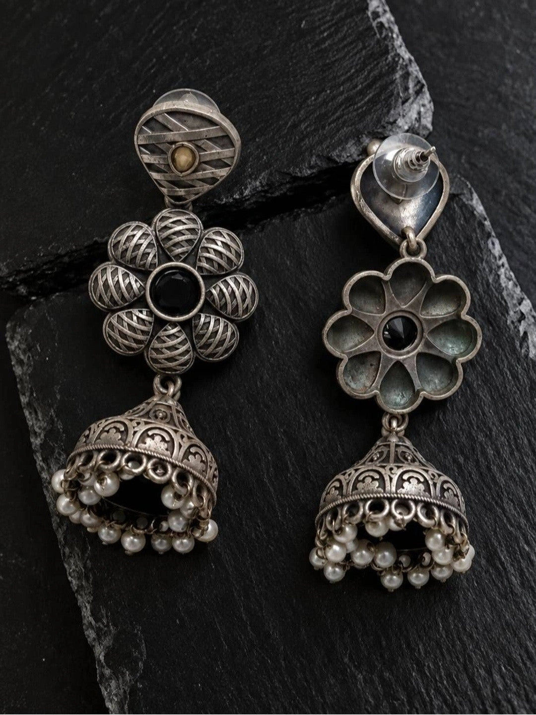 Front and back view of oxidised silver floral jhumka earrings on dark slate surface