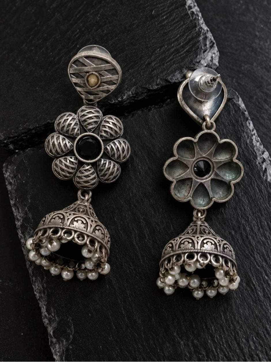 Front and back view of oxidised silver floral jhumka earrings on dark slate surface