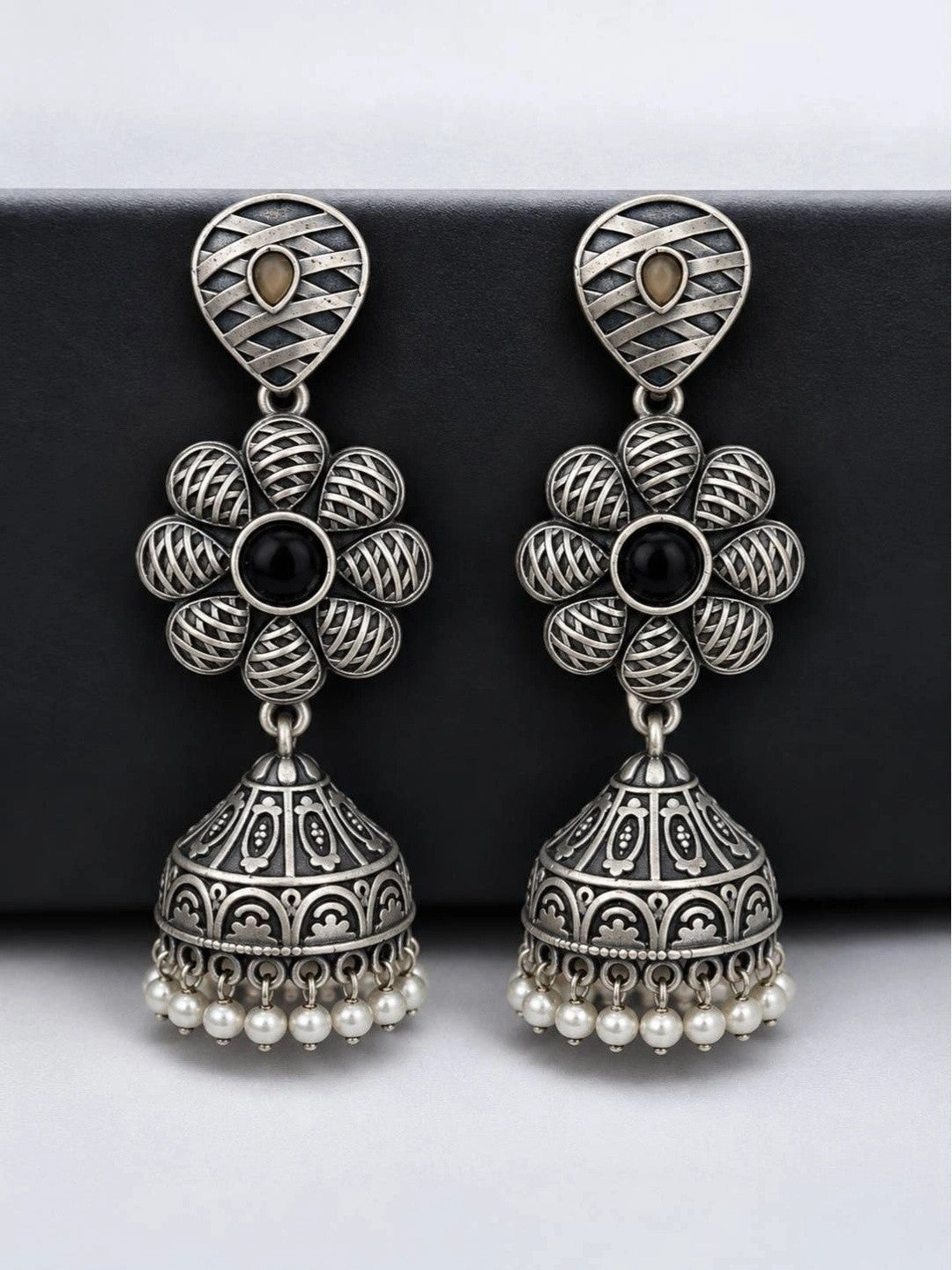 Pair of oxidised silver floral jhumka earrings with engraved dome and pearl beads on dark board