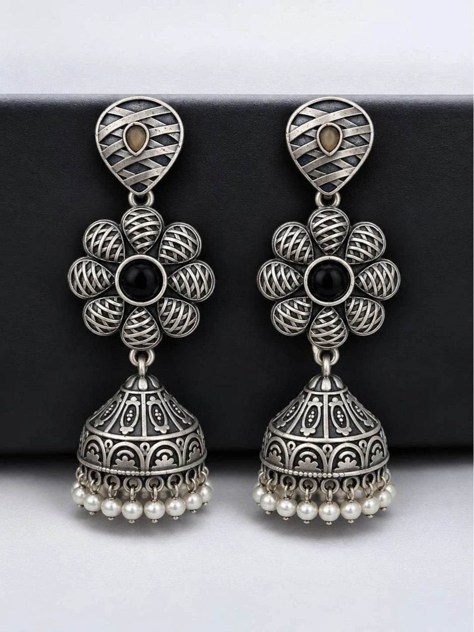 Pair of oxidised silver floral jhumka earrings with engraved dome and pearl beads on dark board