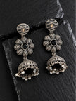 Two oxidised silver jhumka earrings with woven petal flower and pearl drop detail on slate