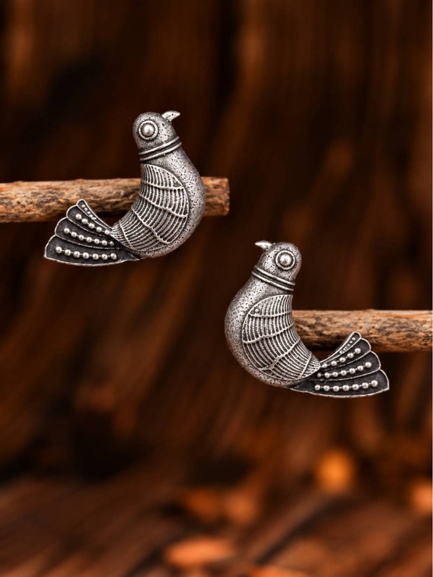 Pair of oxidised silver bird stud earrings perched on a wooden branch against a warm brown background