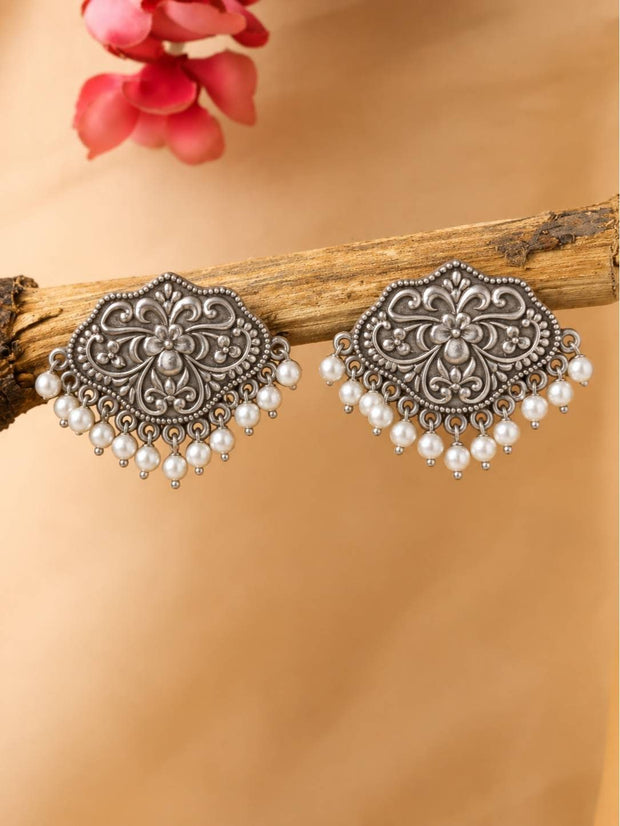 Pair of oxidised silver floral stud earrings with white pearl drop fringe displayed on a wooden branch