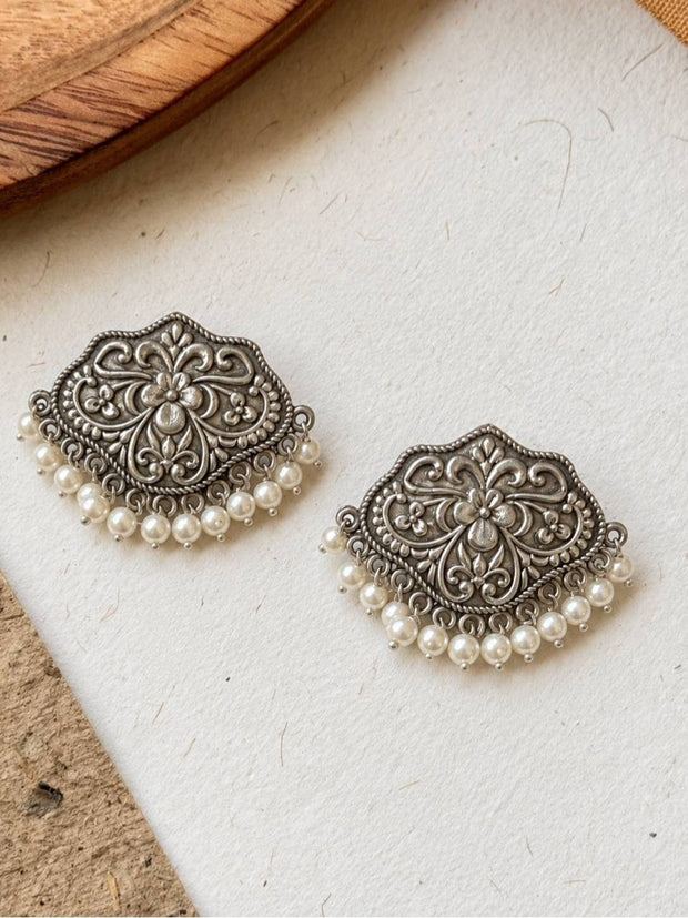 Front view of oxidised silver medallion stud earrings with pearl drops laid flat on a white surface