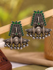 Pair of oxidised silver chandbali earrings with green glass stones and ghungroo drops displayed on a wooden stand