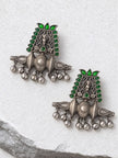 Front view of two oxidised silver deity chandbali earrings with green teardrop stones laid on white stone surface