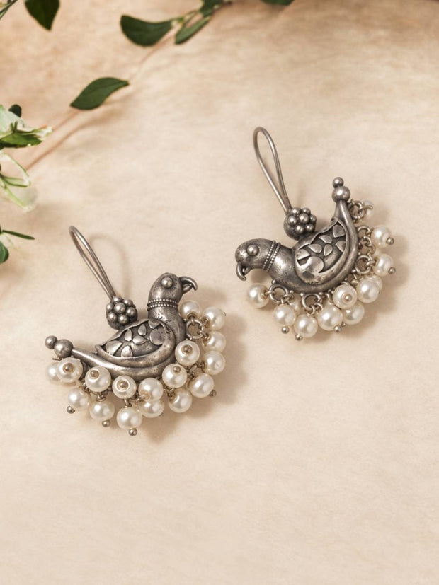 Front view of a pair of oxidised silver parrot chandbali earrings with white pearl bead drops on a cream background