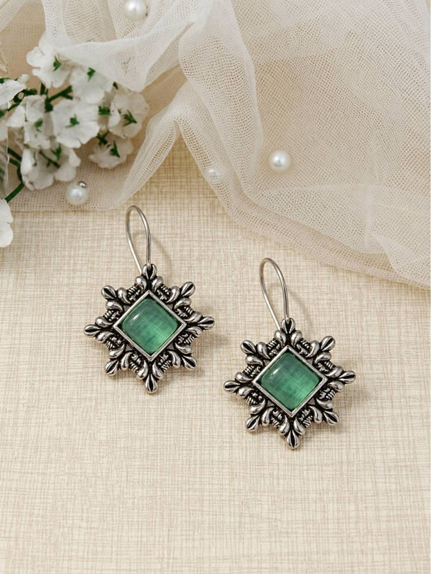 Pair of oxidised silver square dangle earrings with green cat-eye stone centres on a cream fabric background