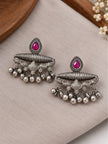 Pair of oxidised silver chandbali earrings with fuchsia stone and ghungroo drops laid flat on grey linen surface