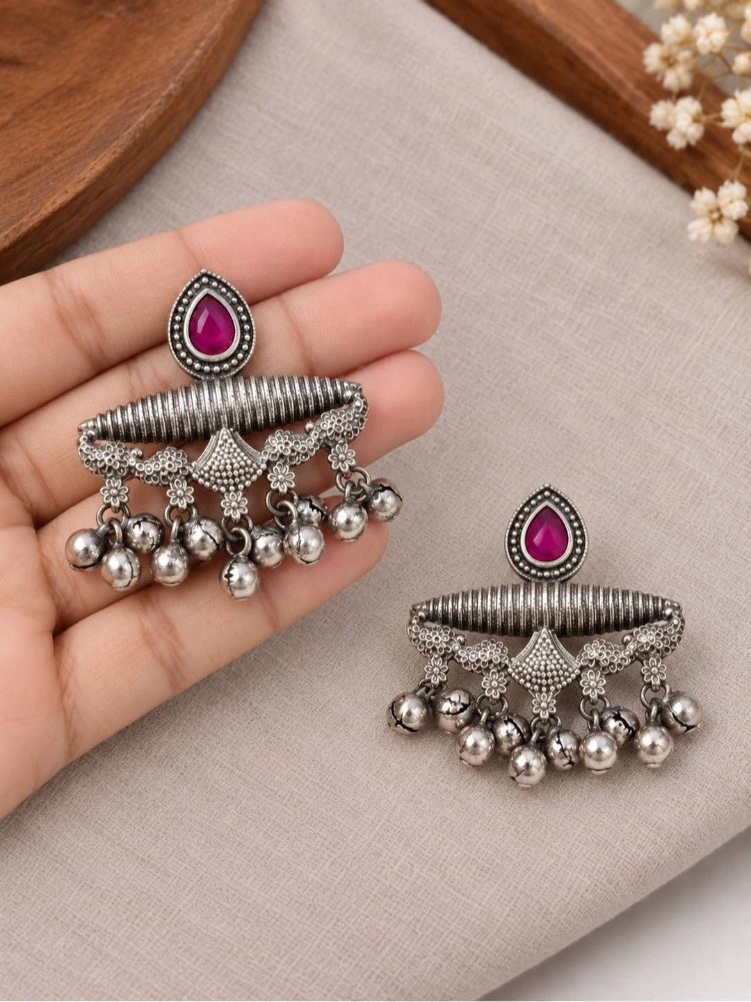Hand holding one oxidised silver chandbali earring showing size scale with second earring resting on grey fabric below
