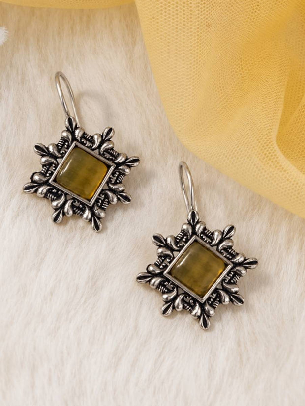 Pair of oxidised silver square drop earrings with olive-green stone centres laid flat on white fur