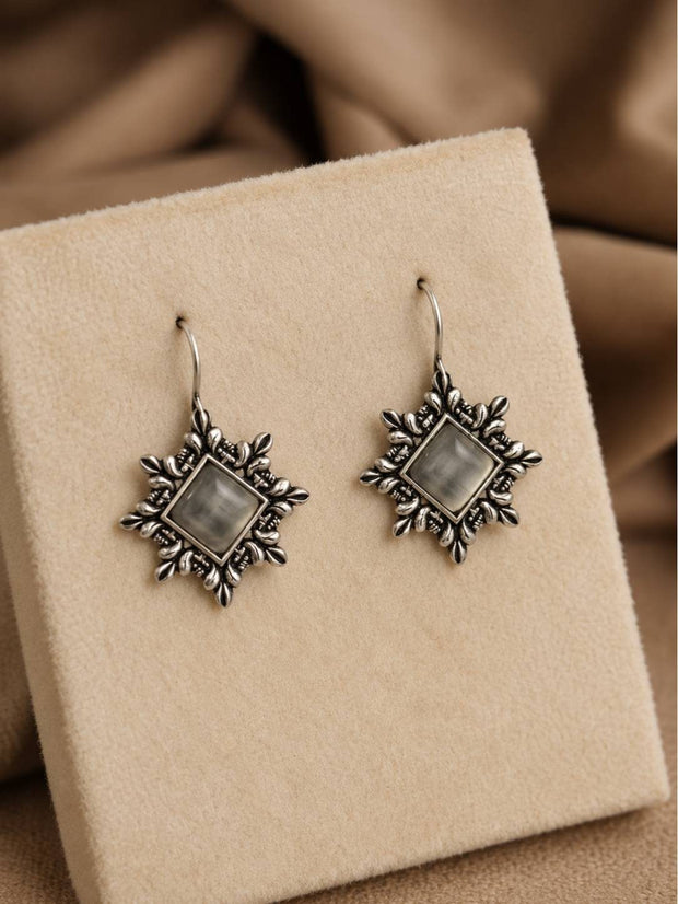 Pair of oxidised silver starburst hook earrings with grey stone centres displayed on a beige velvet jewellery box