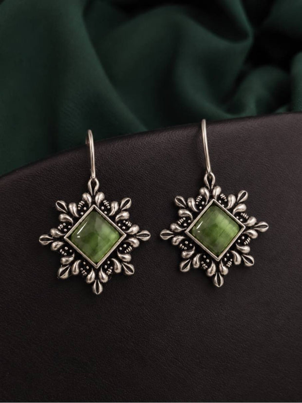 Pair of oxidised silver floral hook earrings with square green cat-eye stones on dark leather and green fabric background