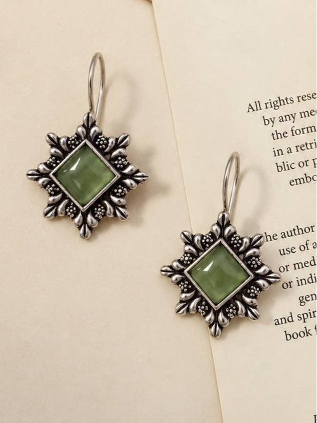 Two oxidised silver floral earrings with green stone centres displayed flat on an open book page