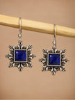 Pair of oxidised silver square drop earrings with blue stone centre hanging on a wooden rod