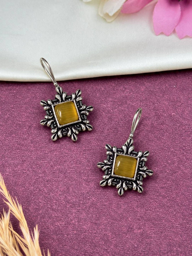 Two oxidised silver floral frame square earrings with yellow stone laid on purple surface with pink flowers