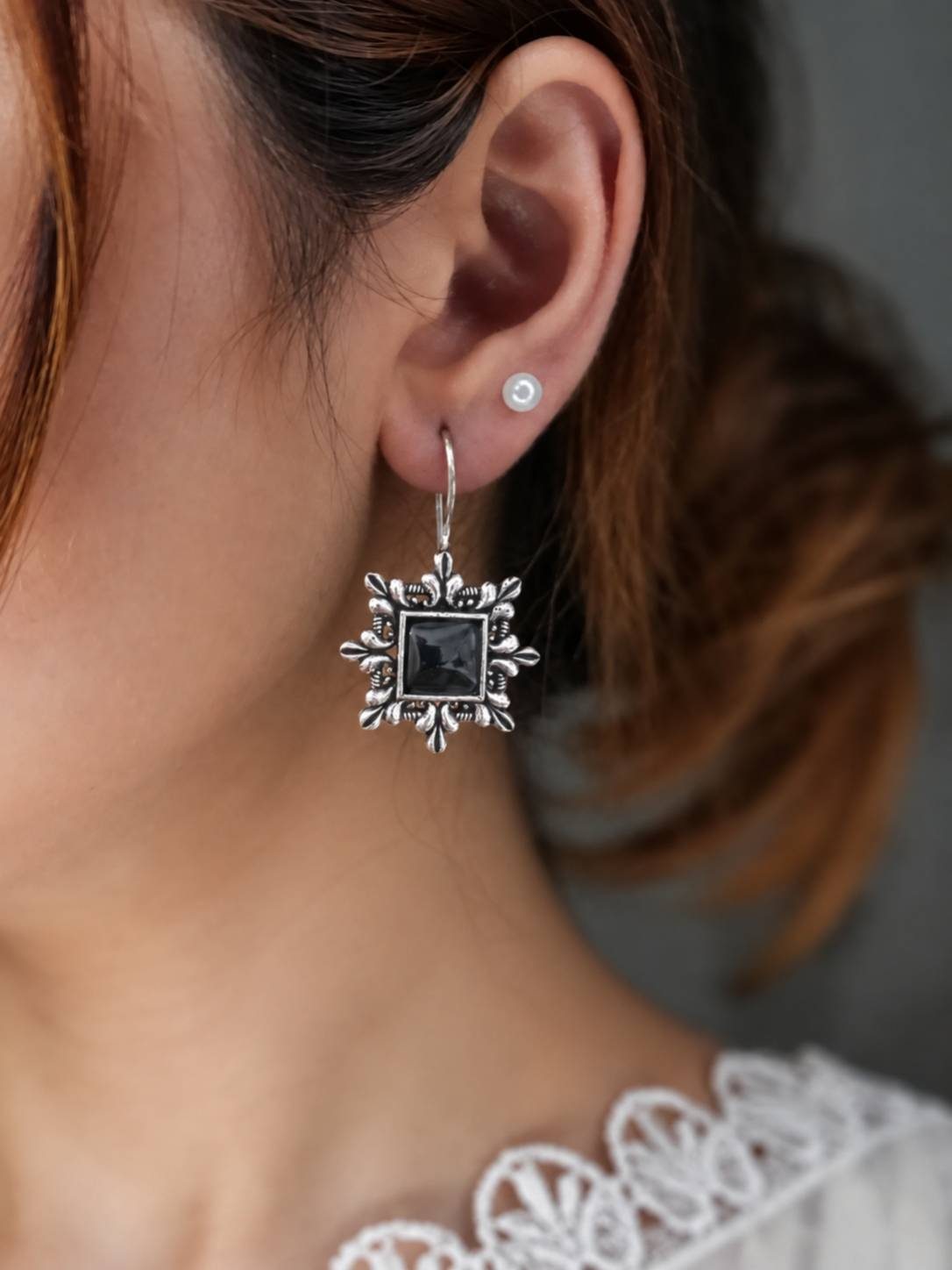 Woman wearing an oxidised silver square drop earring with black stone on her right ear alongside a small pearl stud