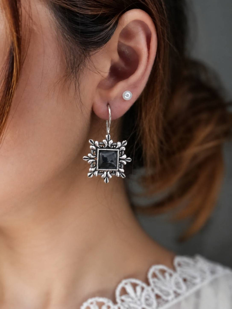 Woman wearing an oxidised silver square drop earring with black stone on her right ear alongside a small pearl stud