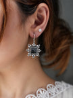 Woman wearing an oxidised silver square drop earring with black stone on her right ear alongside a small pearl stud