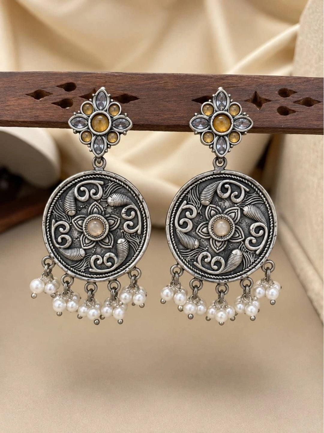 Pair of oxidised silver chandbali earrings displayed on wooden rack showing lotus motif and pearl drops