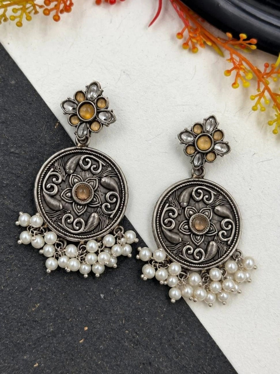 Close-up of oxidised silver chandbali earrings with amber stone flower stud top and white pearl drop fringe