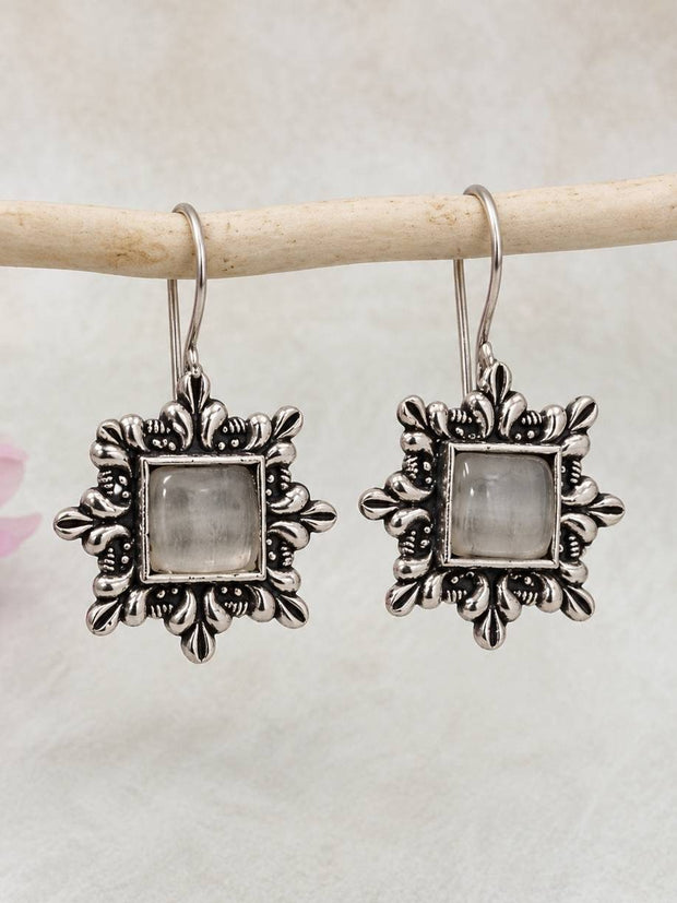 Pair of oxidised silver square drop earrings with grey cabochon stone hanging on a wooden rod