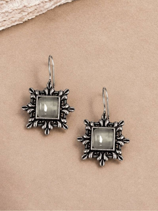 Two oxidised silver square earrings with floral border laid flat on a beige surface