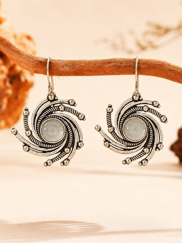 Pair of oxidised silver spiral drop earrings with green cabochon centres hanging from a rustic wooden branch