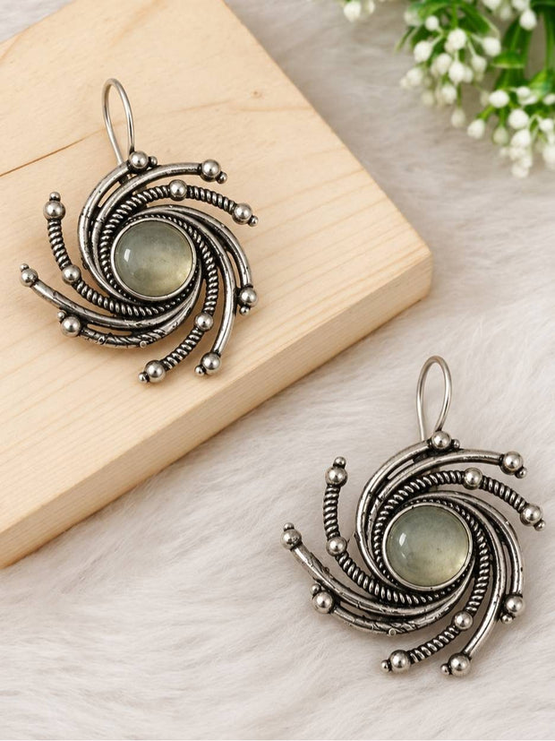 Two oxidised silver spiral earrings displayed on a wooden board and white fur surface with floral background