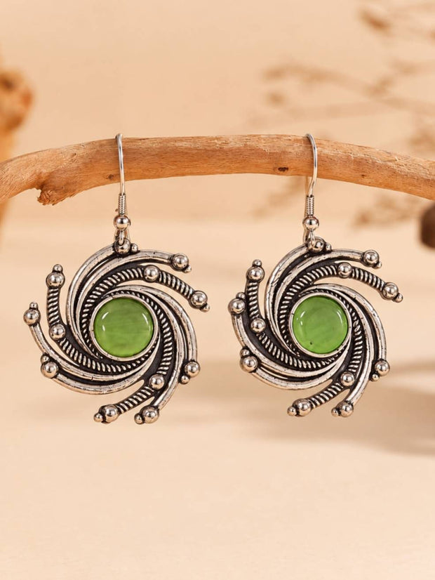 Pair of oxidised silver spiral drop earrings with green cabochon centres displayed on a wooden branch