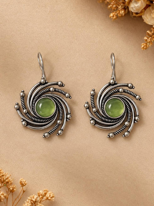 Front view of both oxidised silver swirl earrings with green stone centres laid flat on a beige surface