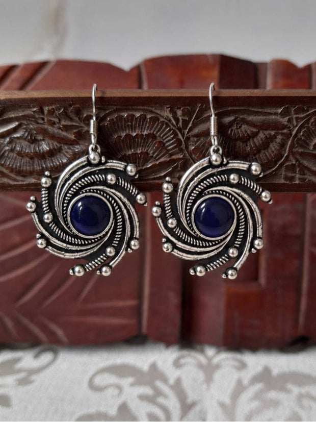 Pair of oxidised silver spiral drop earrings with blue cabochon centre displayed against a carved wooden jewellery box