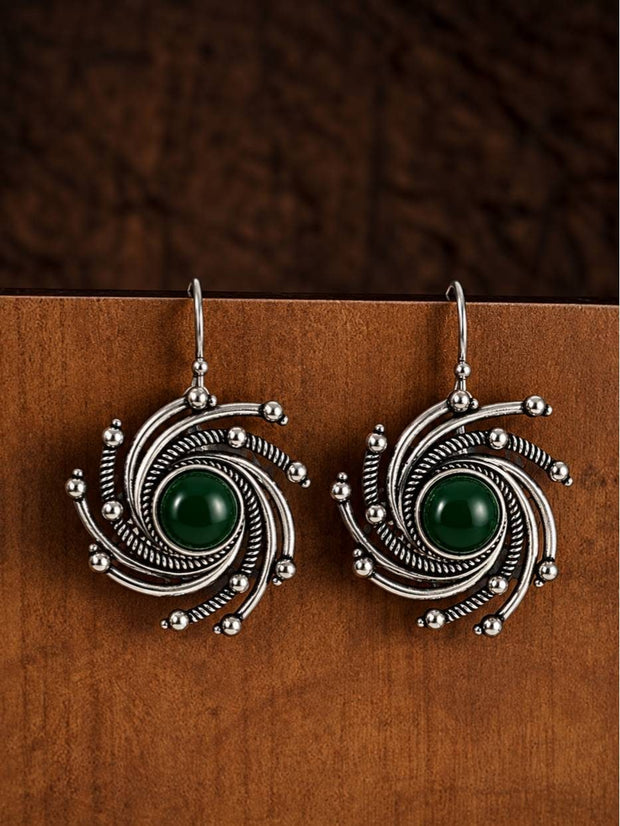 Pair of oxidised silver spiral drop earrings with green cabochon centres displayed on a wooden card