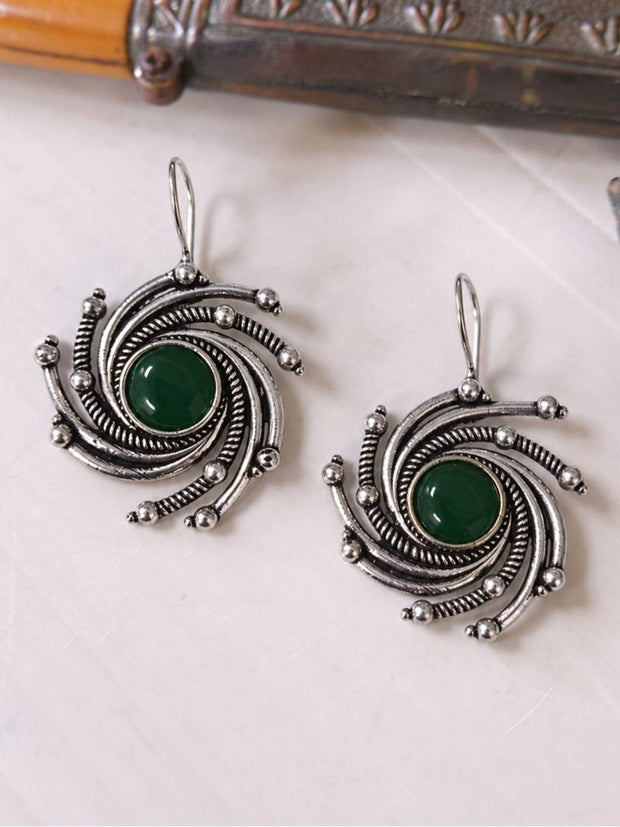 Front view of oxidised silver swirl earrings with green stone centres laid flat on a white surface