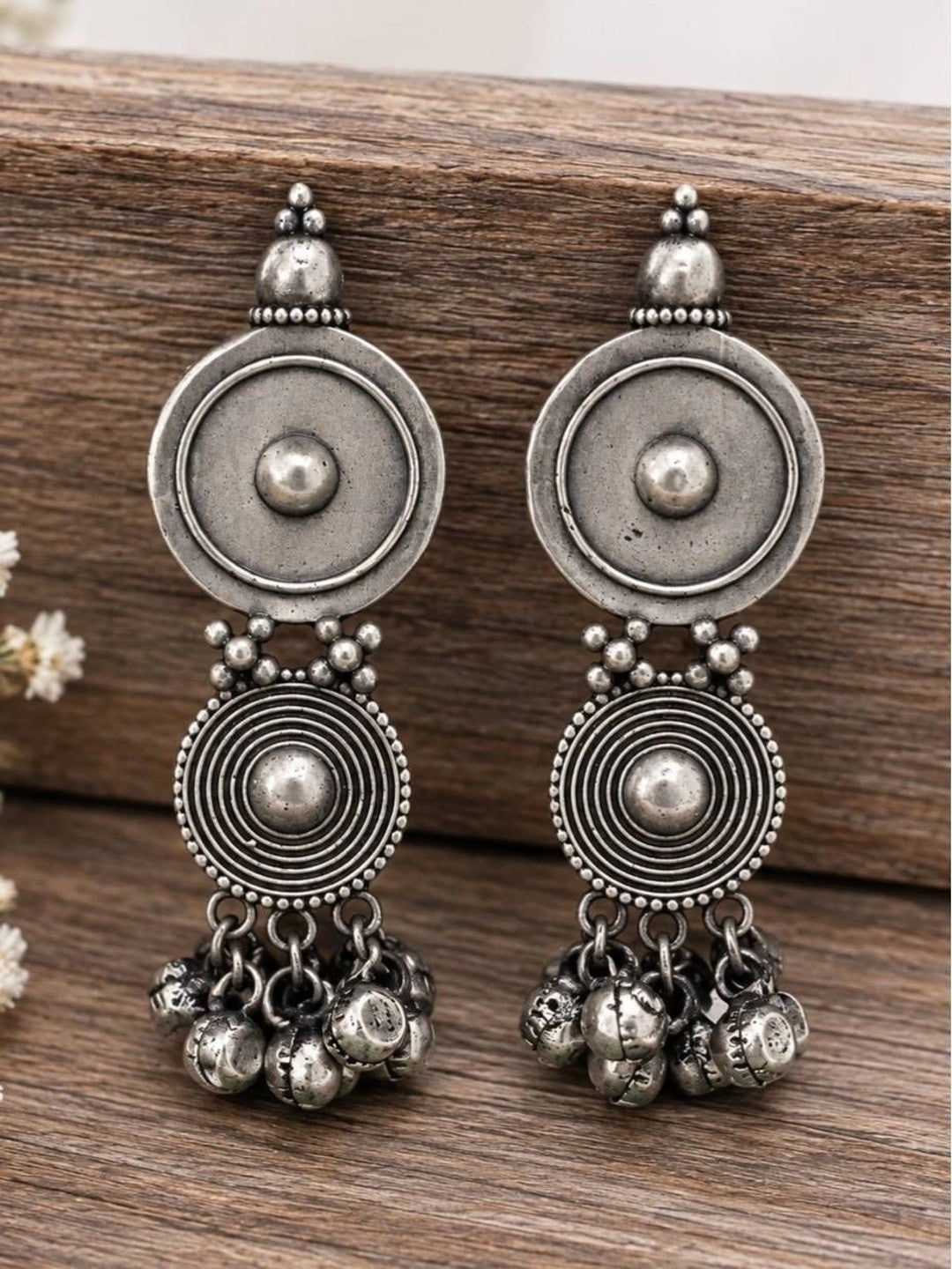 Pair of oxidised silver concentric disc earrings with bell clusters on wooden surface