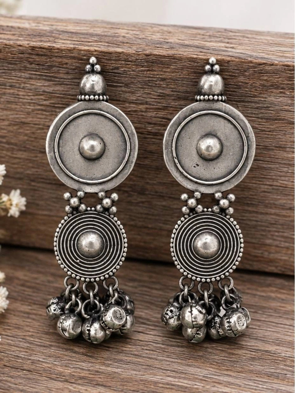 Pair of oxidised silver concentric disc earrings with bell clusters on wooden surface