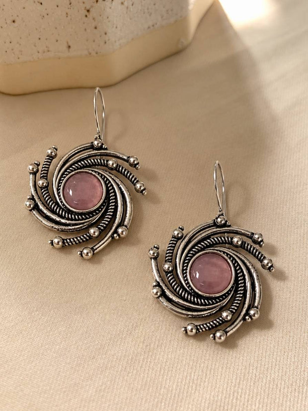 Two oxidised silver spiral earrings with pink stone centres lying flat on a cream fabric surface