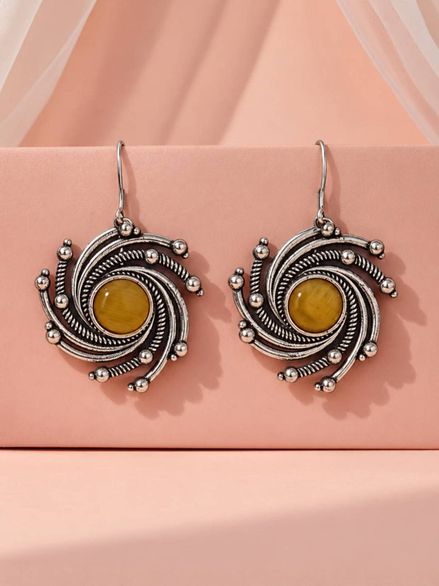 Pair of oxidised silver spiral drop earrings with yellow cabochon stone on a pink display block