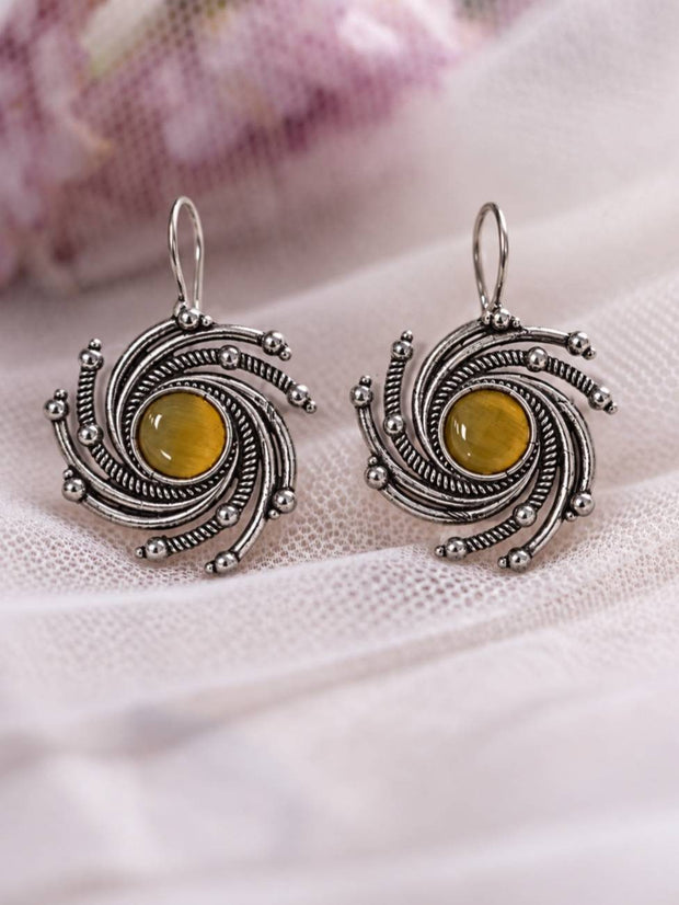 Two oxidised silver swirl earrings with yellow centre stones laid flat on white fabric with pink flowers in background