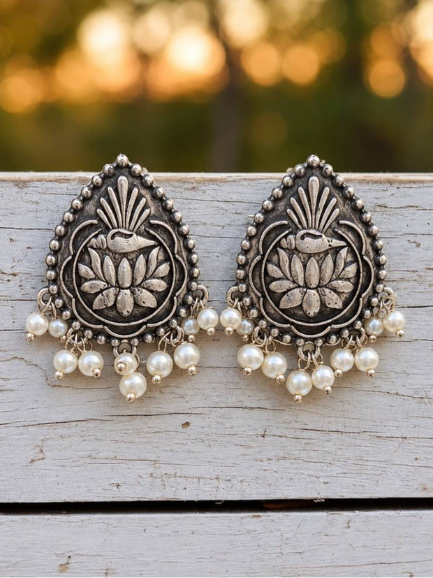 Pair of oxidised silver lotus stud earrings with pearl drops resting on a weathered white wooden surface outdoors