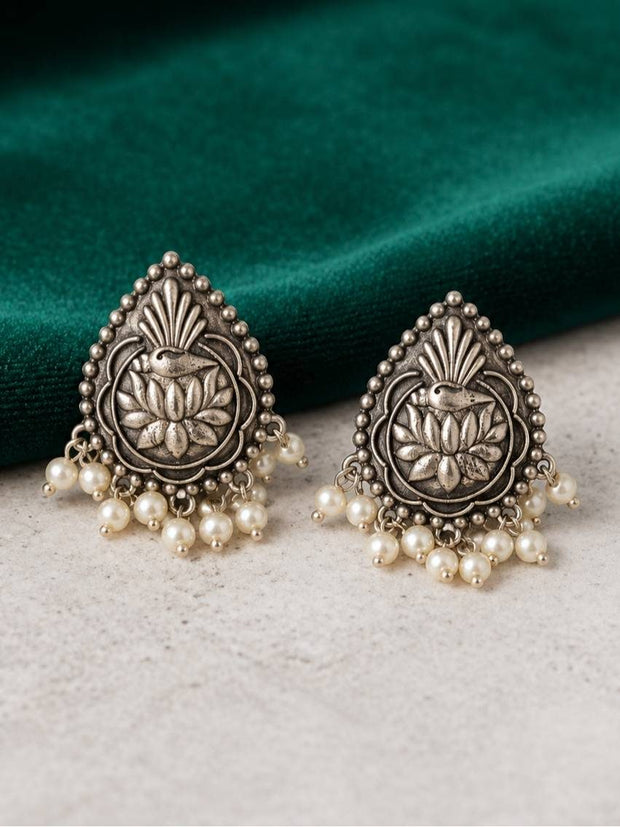 Front view of two oxidised silver lotus earrings with pearl fringe displayed on a green velvet fabric